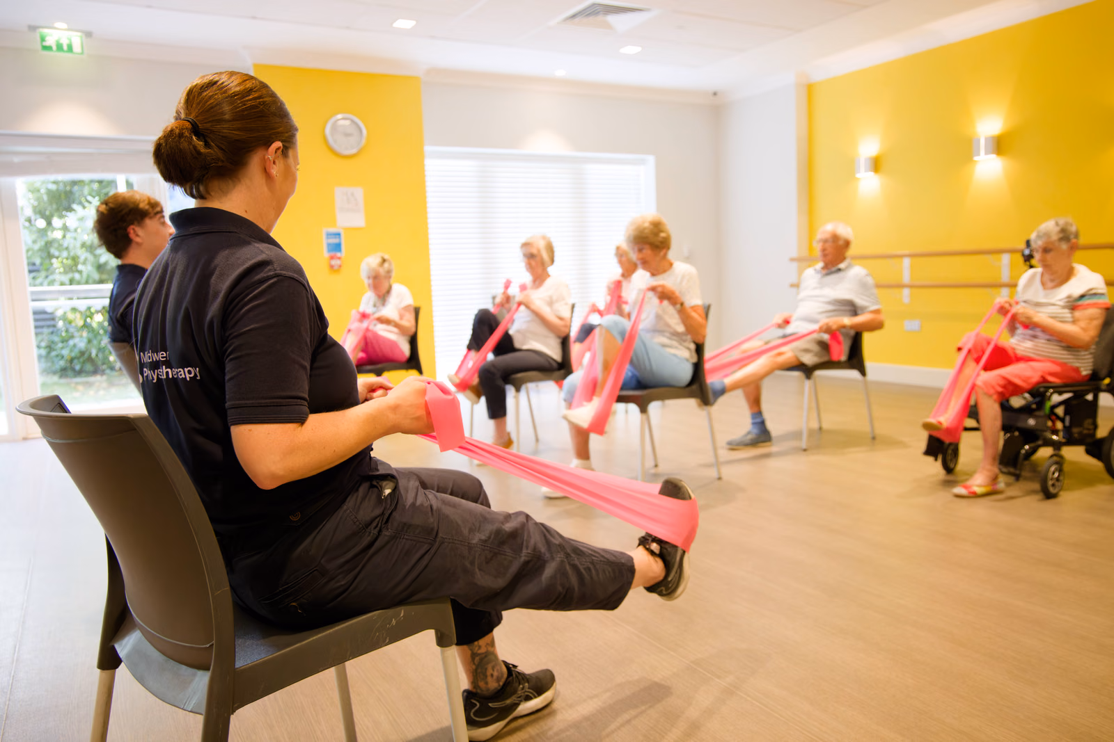 A physiotherapist leading a seated group exercise class using resistance bands